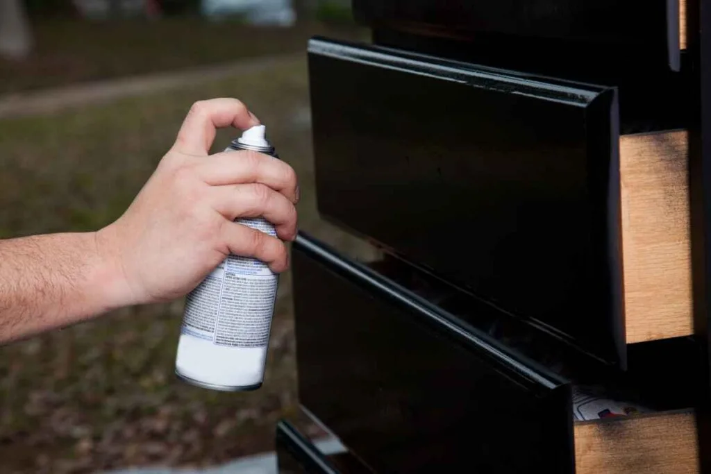 Spraying a coat of polyurethane on a black chest