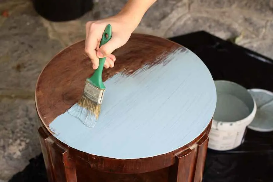 Hand applying chalk paint to furniture with a brush.