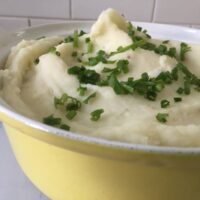 Mashed potatoes in yellow serving bowl with chive topping