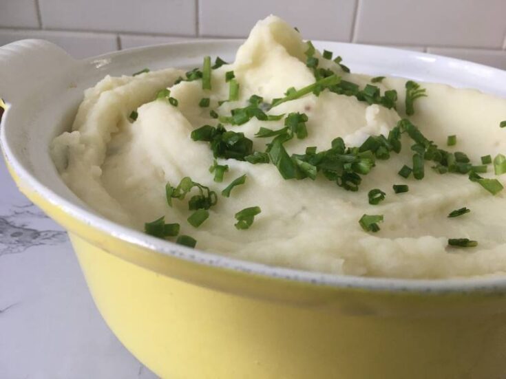 Mashed potatoes in yellow serving bowl with chive topping