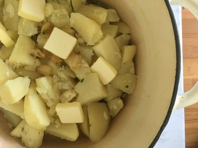 Cooked and drained potatoes in a pot with butter and roasted garlic
