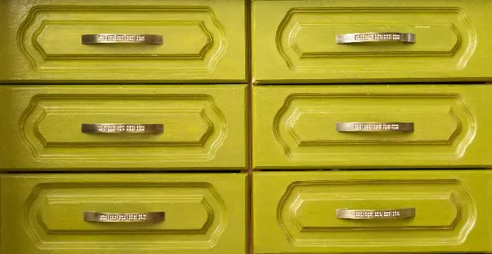 Closeup of a yellow green painted dresser with carved panel drawers and metal hardware.