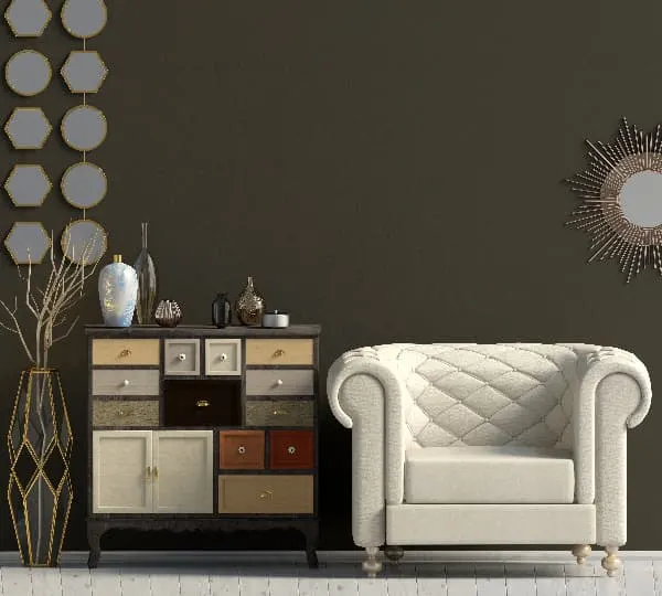 A painted dresser with drawers painted in different colors next to a white upholstered chair, against a dark wall.