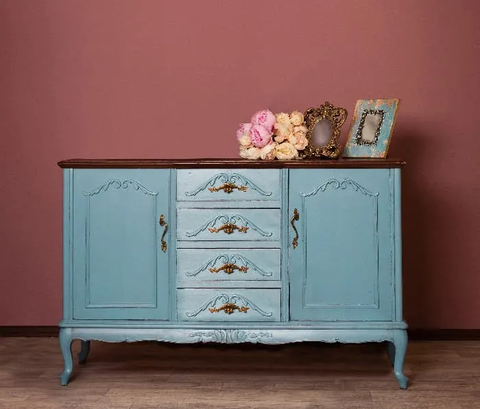 An antique dresser painted light blue against a dark rose wall -- a blue furniture statement piece for the room.