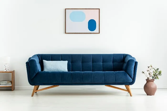 A modern style sofa in navy blue fabric in a white living room with a piece of blue abstract art hung above the sofa -- an example of understate and elegant blue furniture.
