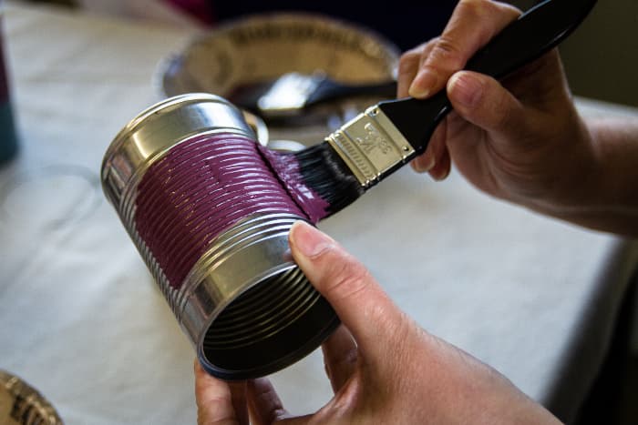 Closeup of hands painting purple chalk paint onto a metal can.