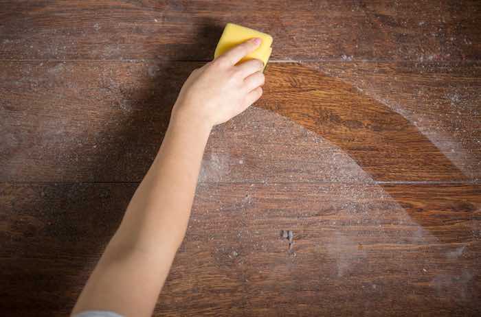 Cleaning dusty wood furniture with a yellow sponge.