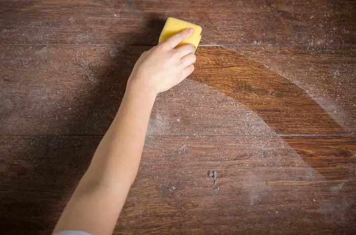 Cleaning dusty wood furniture with a yellow sponge.
