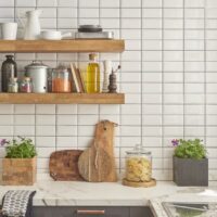 White tiled kitchen accent wall with light brown floating shelves holding kitchen items.