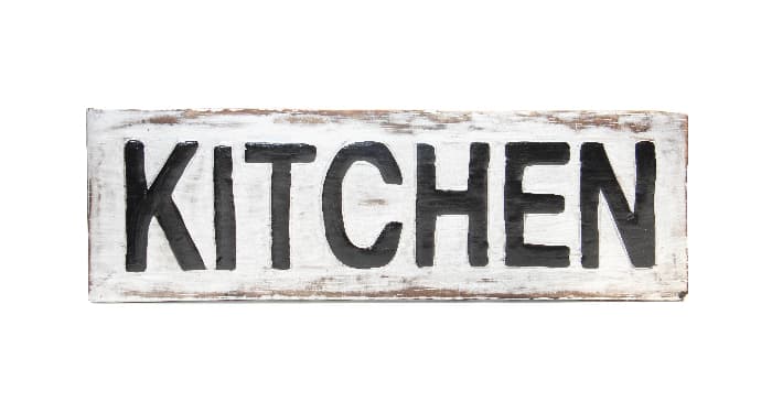 A rustic wooden farmhouse kitchen sign with distressed white paint and "KITCHEN" in dark, bold lettering.