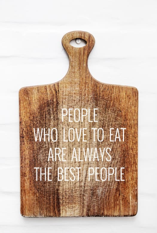 A wooden cutting board with the inscription "PEOPLE WHO LOVE TO EAT ARE ALWAYS THE BEST PEOPLE" in white lettering.