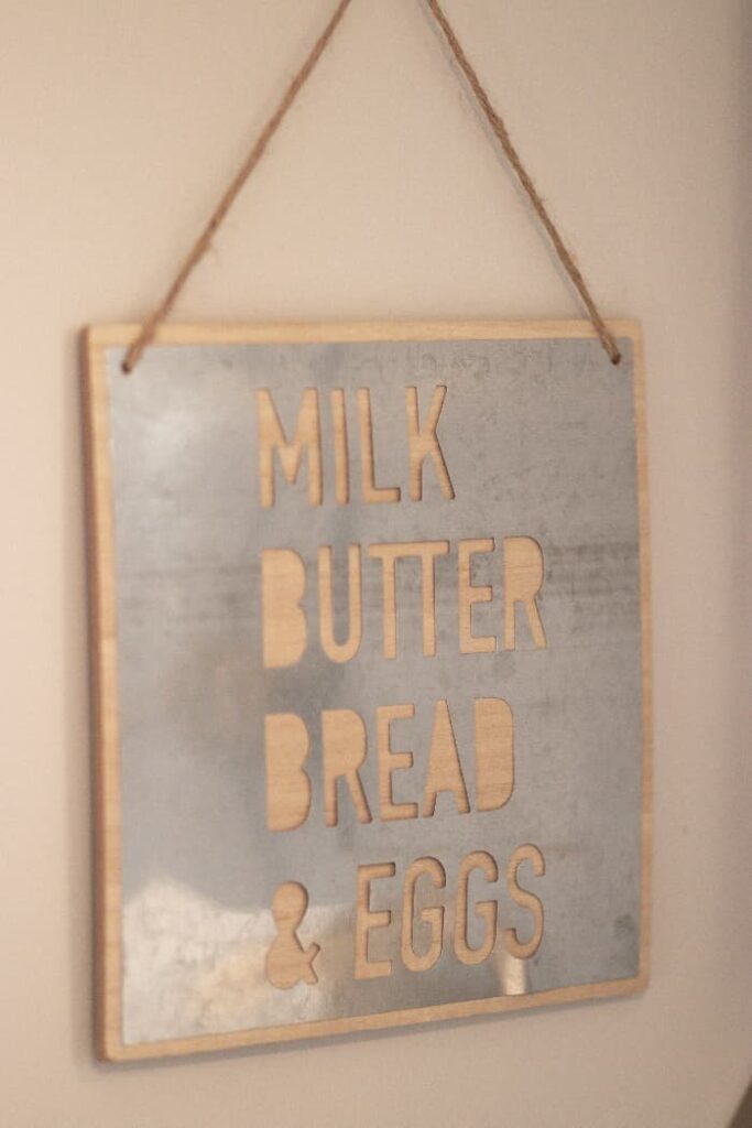 A metal farmhouse sign that reads "MILK BUTTER BREAD & EGGS" that are cut into the surface of the sign.