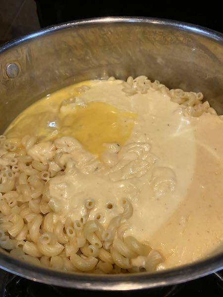Mixing together the beaten eggs, cheese sauce and noodles. 