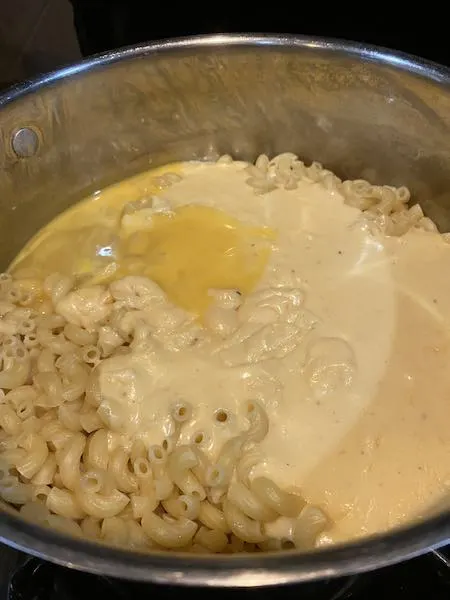 Mixing together the beaten eggs, cheese sauce and noodles.