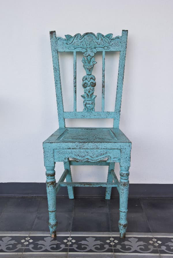 A wooden chair with carved ornate detailing and distressed blue paint -- an example of a shabby chic painted chair.