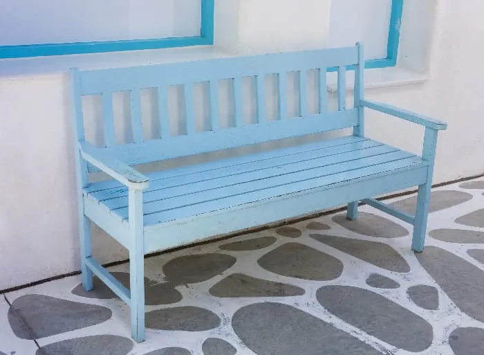 A blue painted bench on a patio next to an exterior wall. While chalk paint is best for indoor projects, it can be used for outdoor items if the paint coat is properly sealed to provide protection from the elements.
