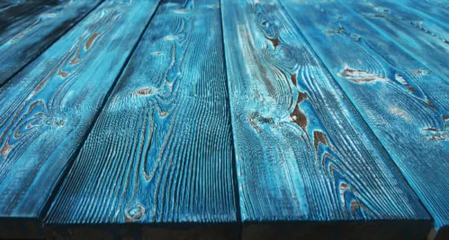 Closeup of a rustic painted table made of planks stained with blue paint.