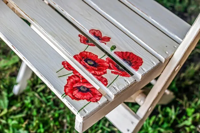 Closeup of a white painted chair seat that has poppies painted in one corner as a decorative detail.