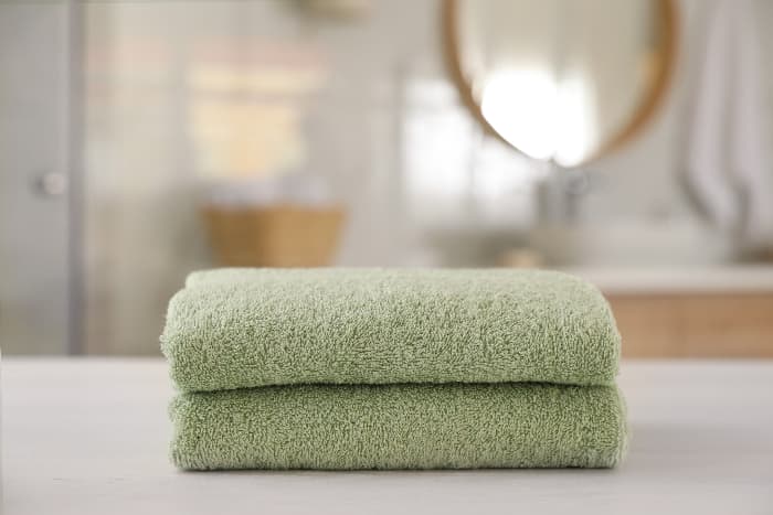 Two stacked towels in pale green color with out of focus modern style bathroom in the background.