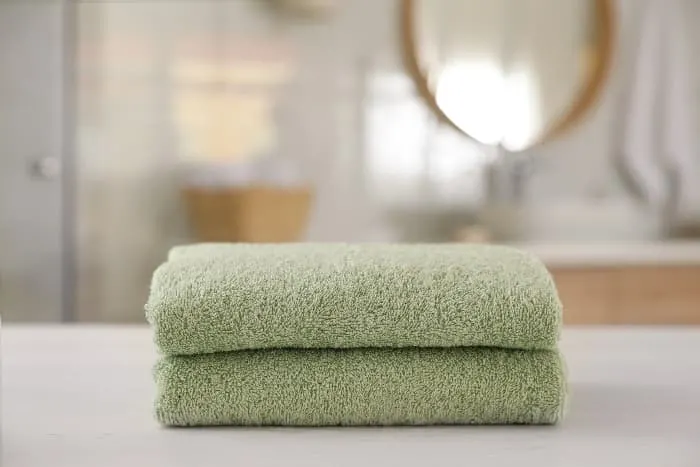 Two stacked towels in pale green color with out of focus modern style bathroom in the background.