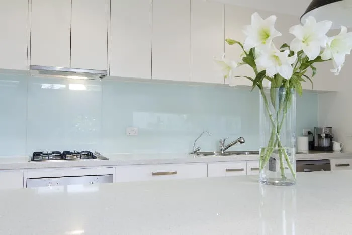 Kitchen with pale green walls, white cabinets, white counters, and stainless appliances with vase of white lilies in foreground.