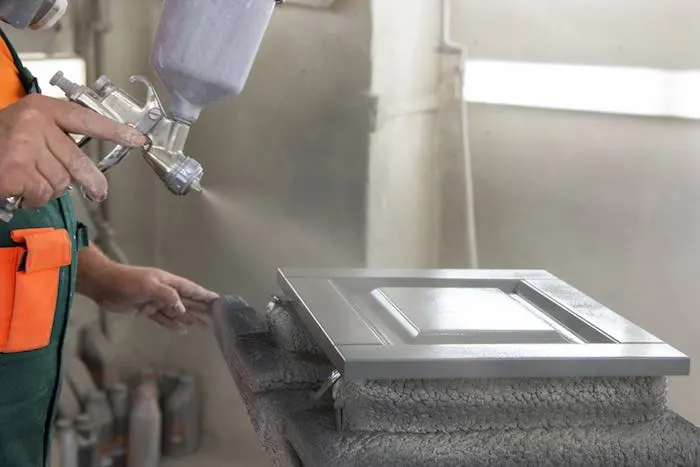 Spray painting a cabinet door from proper distance to avoid blotches.