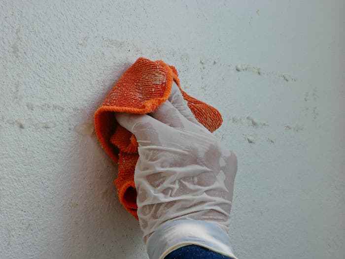 Closeup of vinyl-gloved hand wiping a white painted wall with an orange cloth dipped in solvent -- an example of using solvents to remove chalk paint.