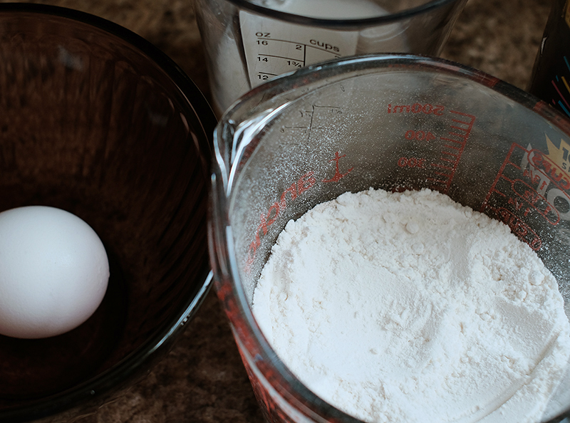 Closeup of a flour in a measuring cup and an egg in a bowl next to the measuring cup.