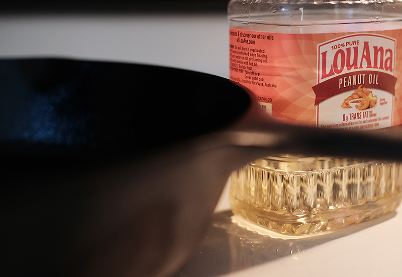 A bottle of peanut oil next to a cast iron pan.