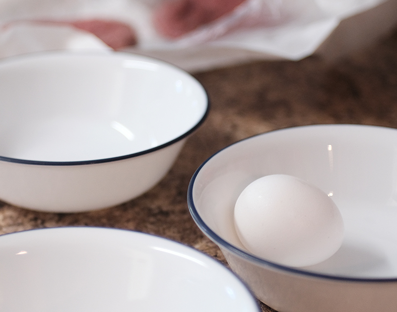 Small white enamel bowls, with an egg sitting in one of them.