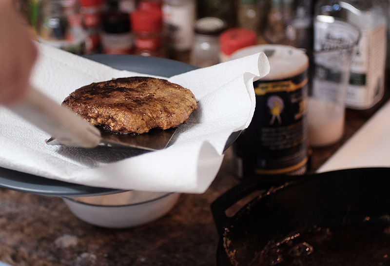 Fried cube steak being placed on paper towels on a plate.