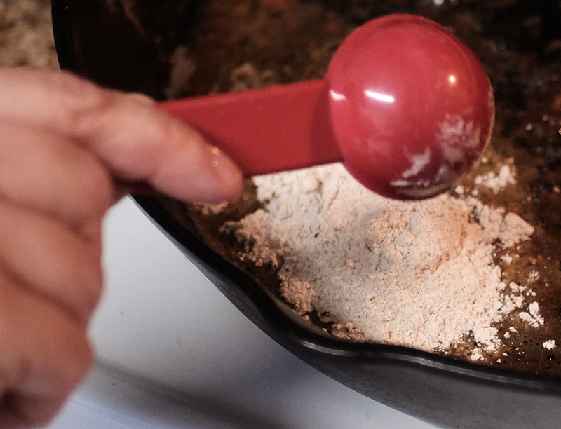 Closeup of flour being added to meat drippings.