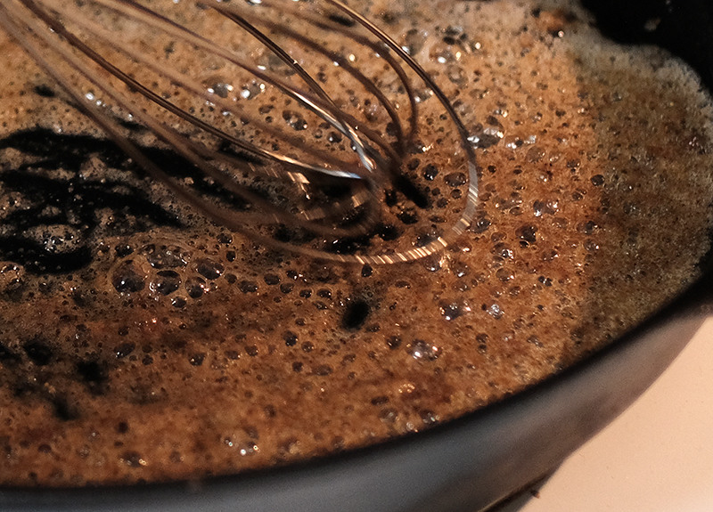 Closeup of a metal whisk stirring gravy meat drippings in a cast iron skillet.
