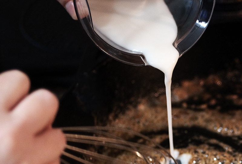 Closeup of milk being whisked into gravy roux.