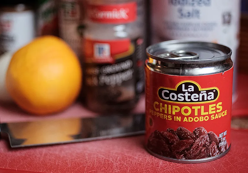 Can of La Costena chipotles with spices and a lemon in the background.