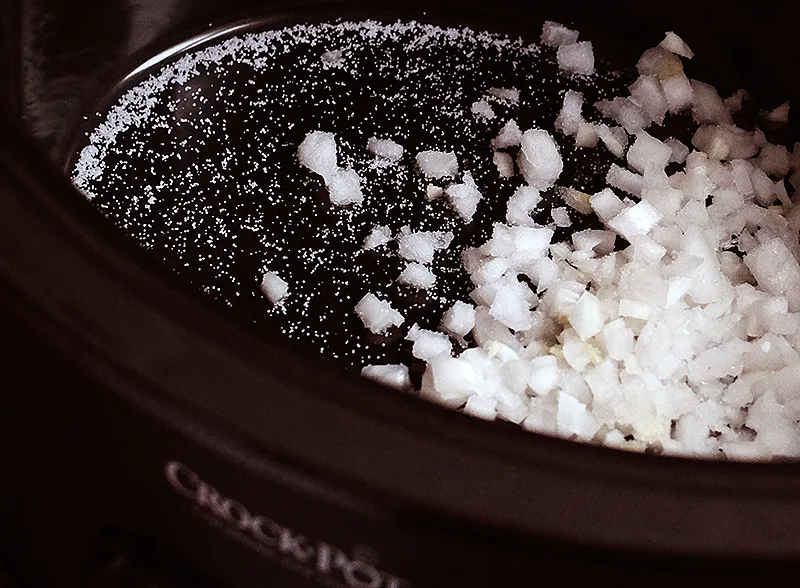 Slow cooker with diced onions and salt in the bottom.