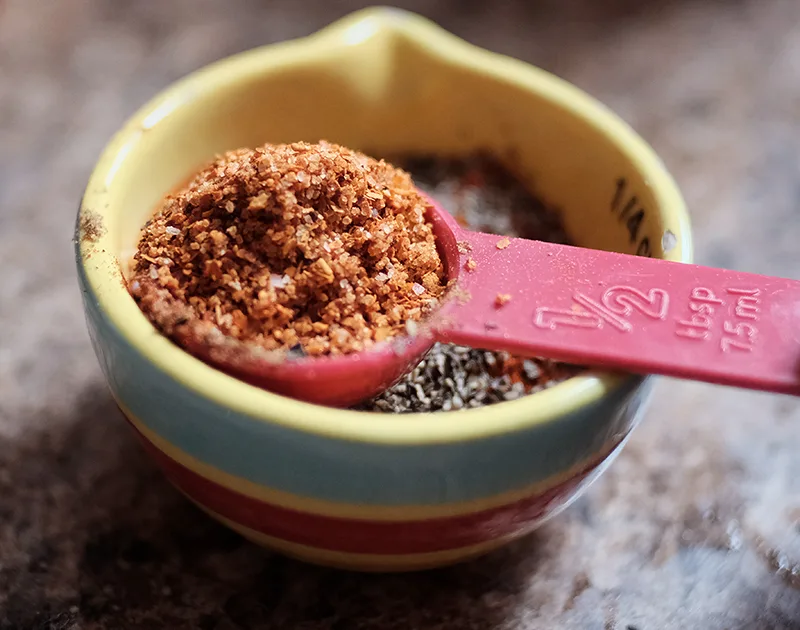 Closeup of measuring spoon of Tajin spice resting in a small bowl of other spices.