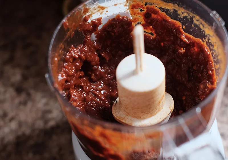 Inside of a food processor bowl with chipotle pepper paste in it.