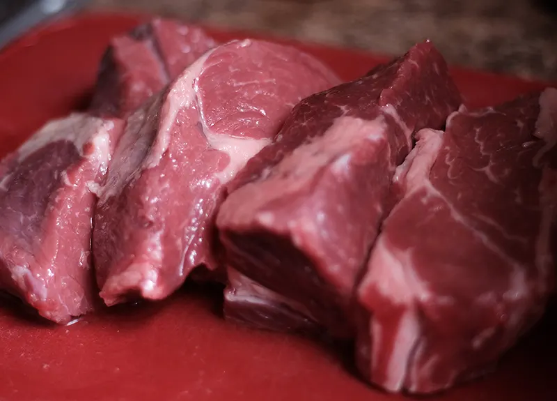 Chuck roast cut into large pieces on a red cutting board.