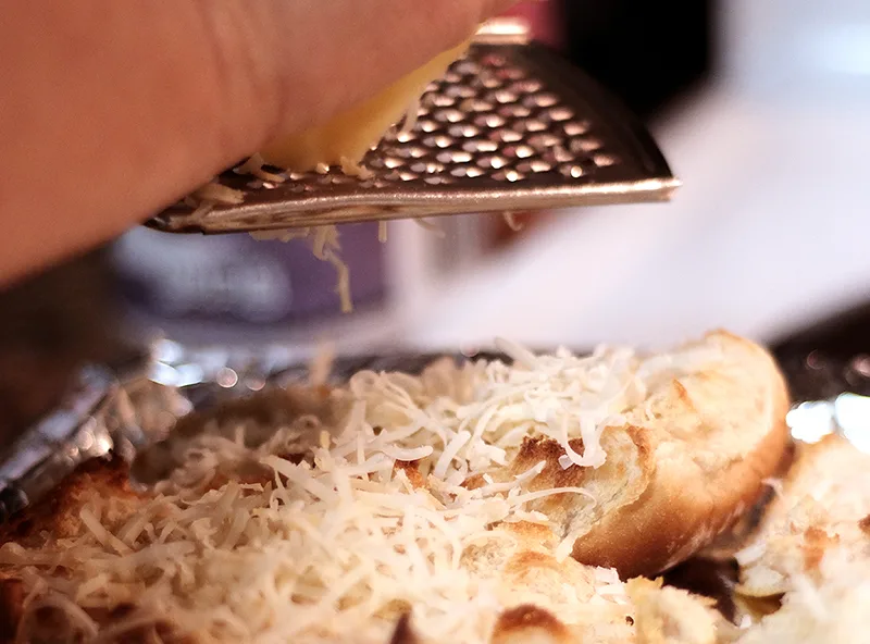 Closeup of hands grating cheese onto slider rolls.