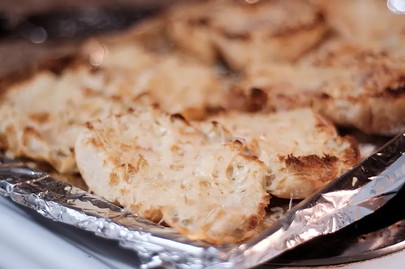 Slider rolls with melted cheese on a foil-covered tray.