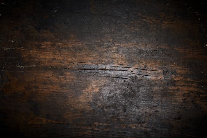 Closeup of wood that appears to be quite old, with cracks, wormholes, gouges, nicks, and dark spots.