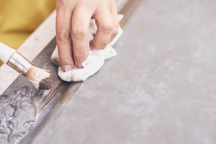 Closeup of a dark glaze being brushed onto decorative details on a piece of furniture.  Using dark glaze or dark wax is a method of how to distress furniture with chalk paint.
