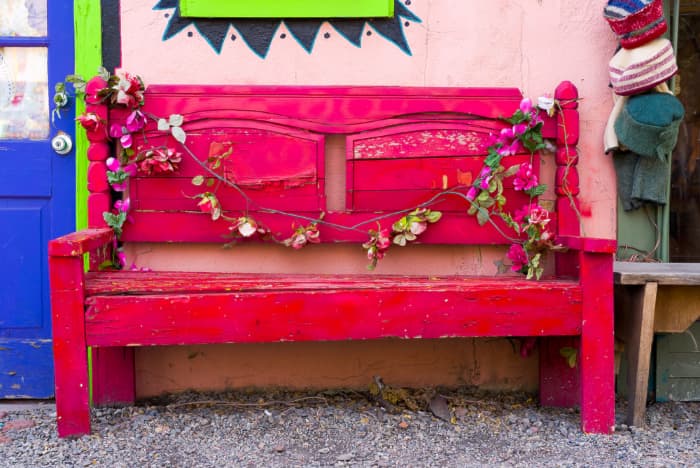 A fuschia colored outdoor bench next to a pink stucco wall.