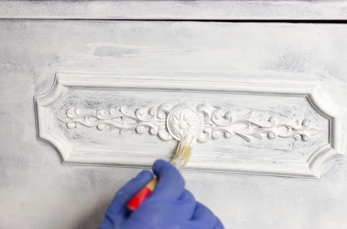 Closeup of hand painting decorative detailing on a piece of furniture. Knowing how to chalk paint furniture may be just what you need to salvage a piece, instead of throwing it away.