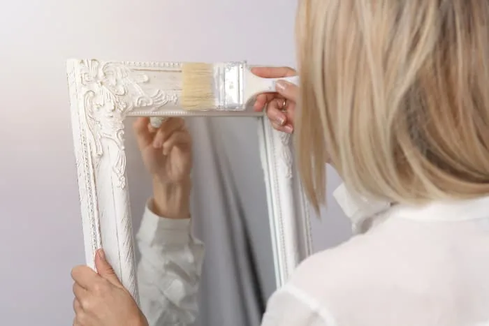 Back view of a woman painting a mirror frame. Until you get the hang of chalk paints, you might want to paint smaller, non-furniture items at first.