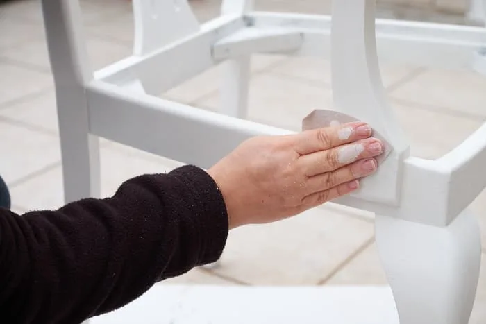 Closeup of woman's hand sanding white painted furniture. Sanding between coats will help give you a smooth finish with chalk paint.