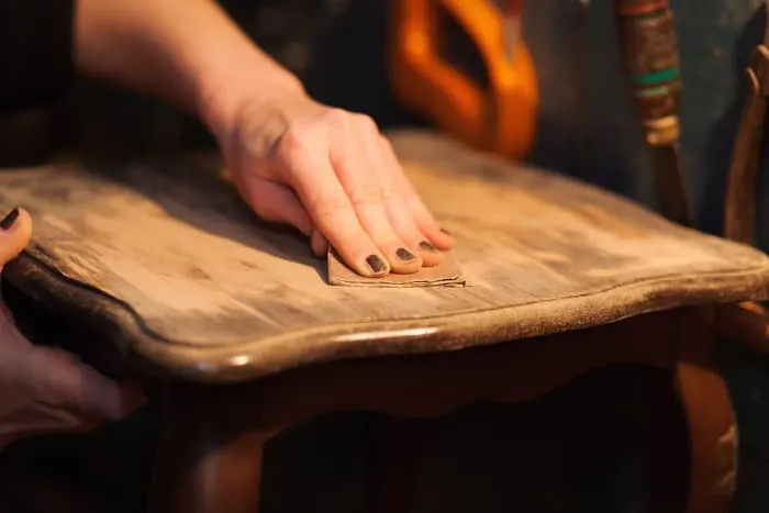 Closeup of woman's hands sanding a wooden tabletop. If there is damage to the surface of a piece, it will affect your ability to get a smooth finish with chalk paint.