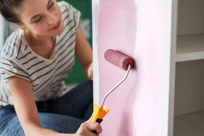 Closeup of a woman using a foam paint roller to apply purple paint to cabinet or bookshelves. Using the right tools helps get a smooth finish with chalk paint.