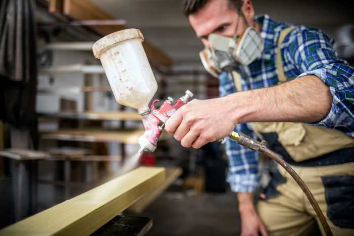 a carpenter using a paint sprayer to paint a piece of wood.